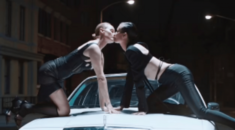 ’90s supermodels Amber Valletta and Shalom Harlow kiss on the hood of a car in the Mugler movie